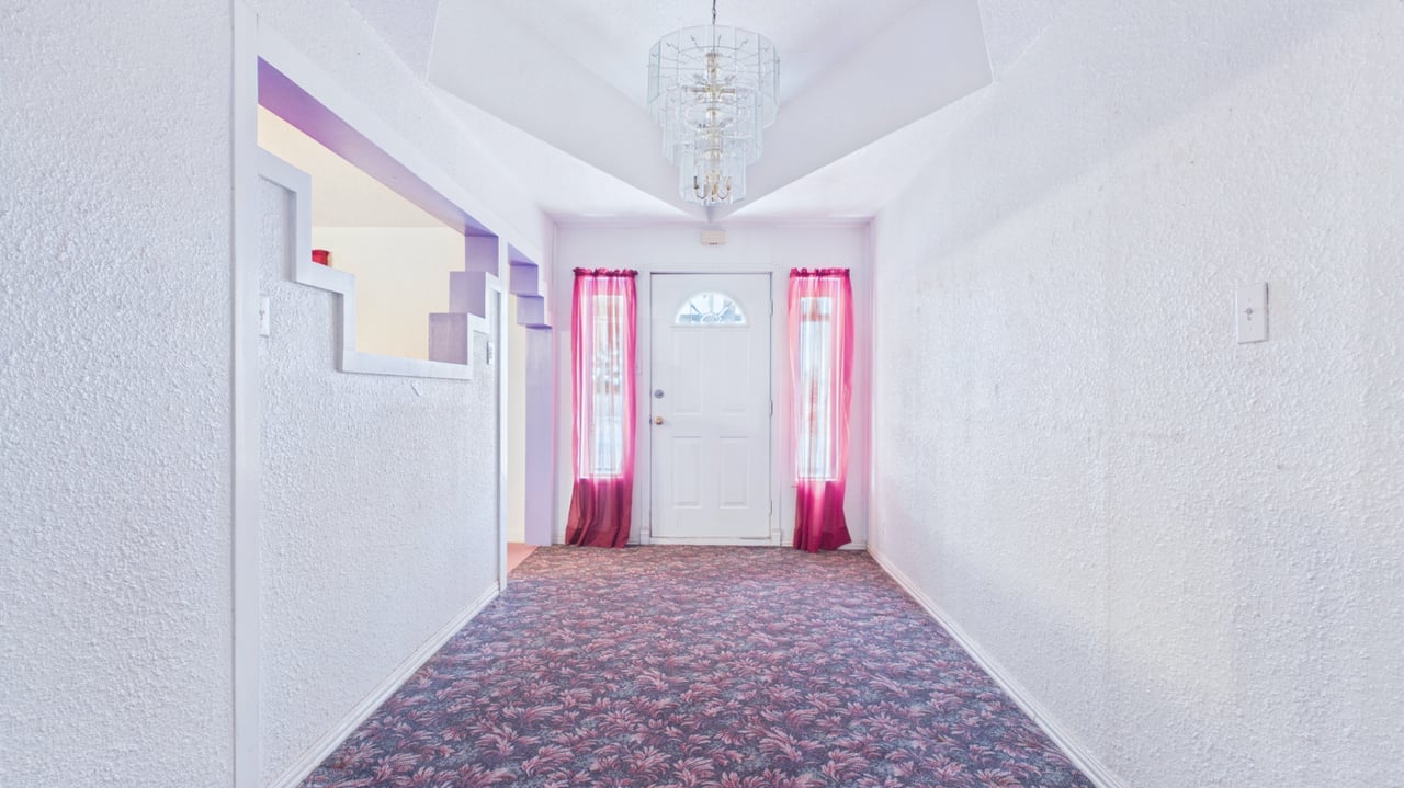 Entry hall with patterned carpet, magenta curtains beside the front door, and a chandelier.