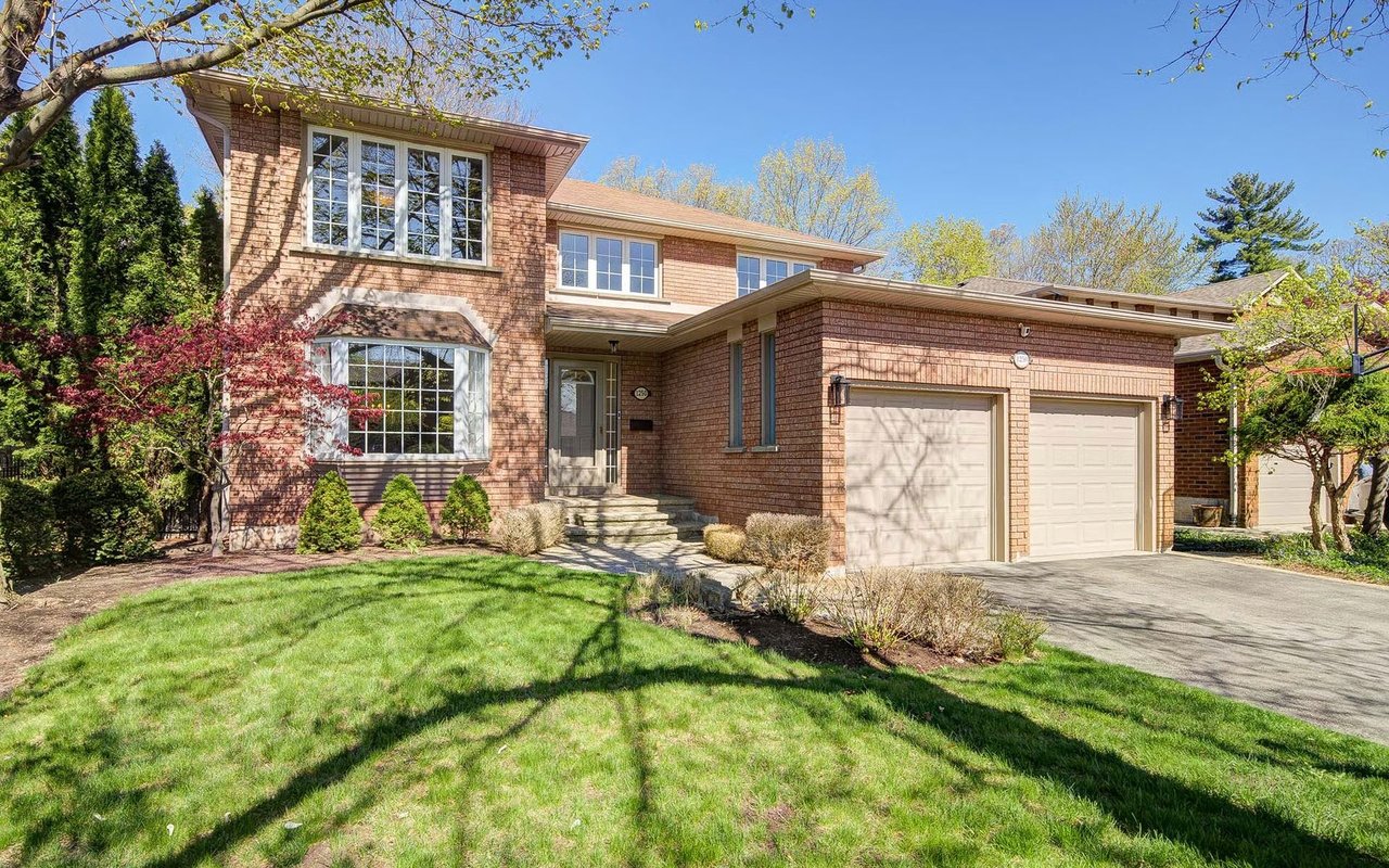 Two-story brick house with a double garage, landscaped lawn, and mature trees.