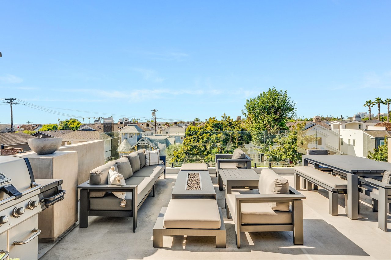 Furnished rooftop deck with a sectional sofa, lounge chairs, and grill overlooking nearby homes.