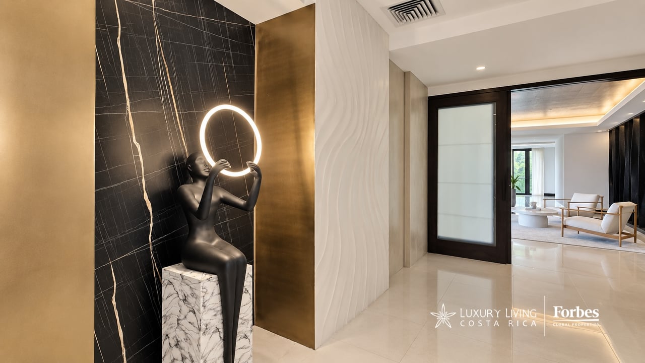 Penthouse entryway with a sculptural figure holding a circular light beside a black marble wall.