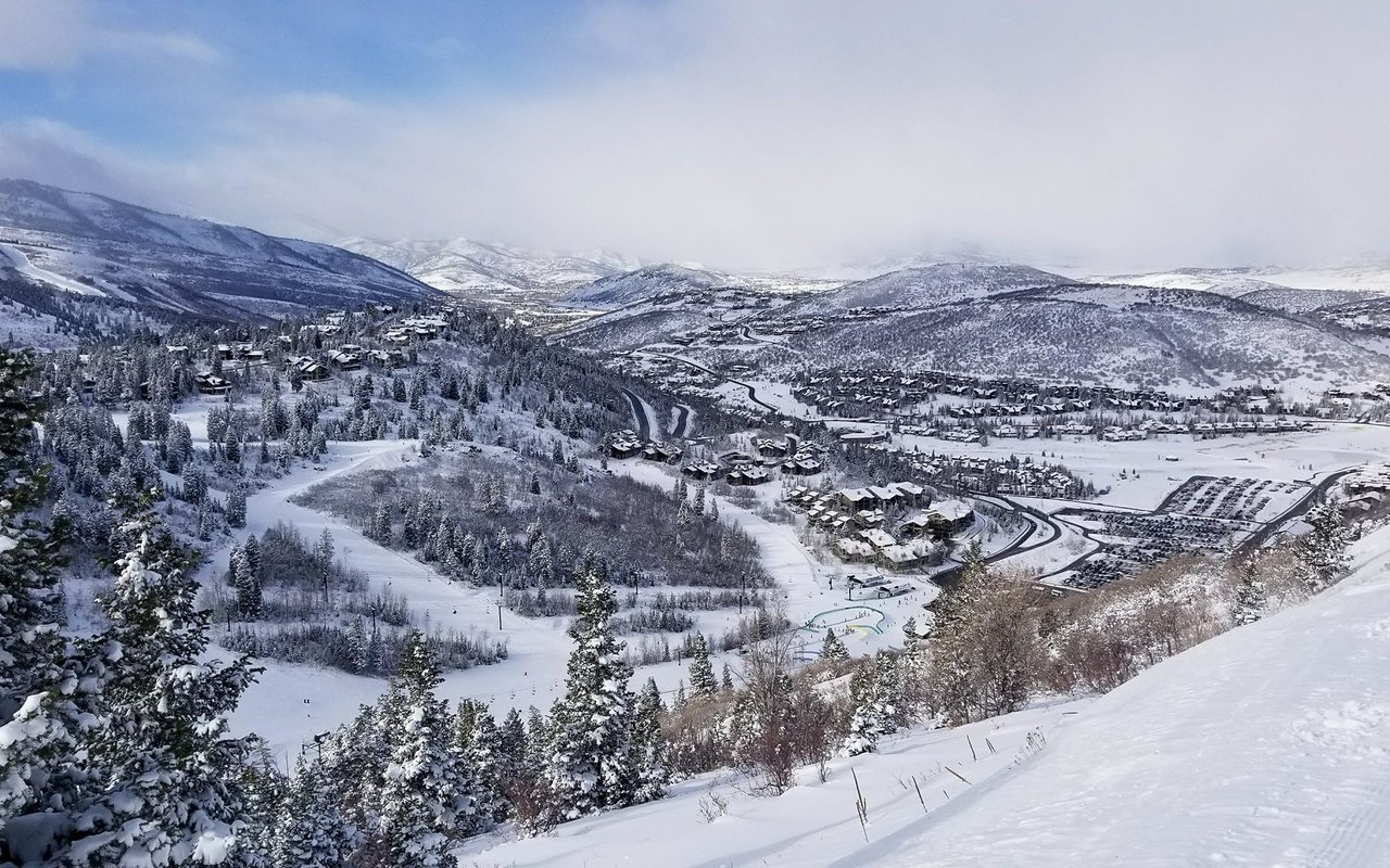 Snow-covered Upper Deer Valley neighborhood with mountain homes, evergreen slopes, and ski trails.