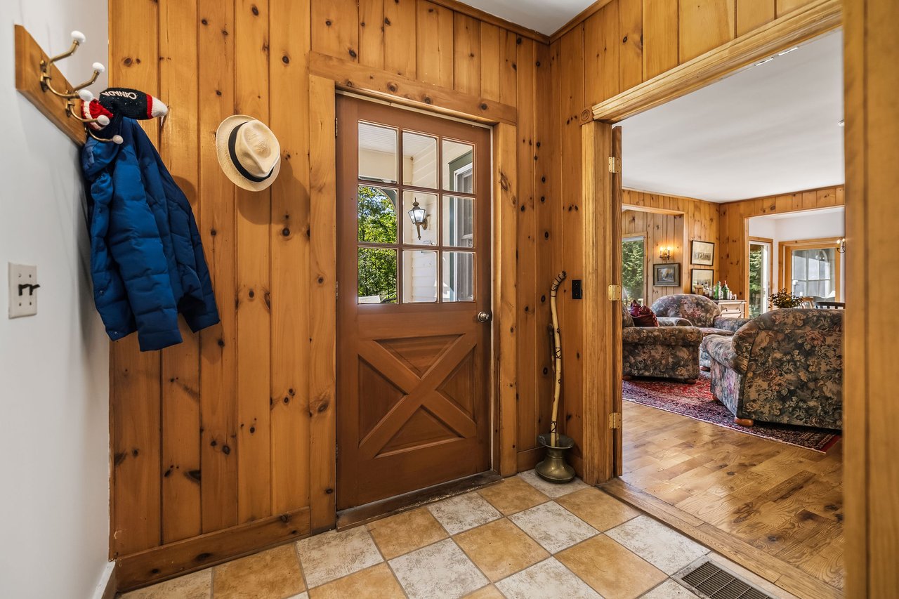 Wood-paneled entryway with a tiled floor and glass-paneled door, opening into a furnished living room.