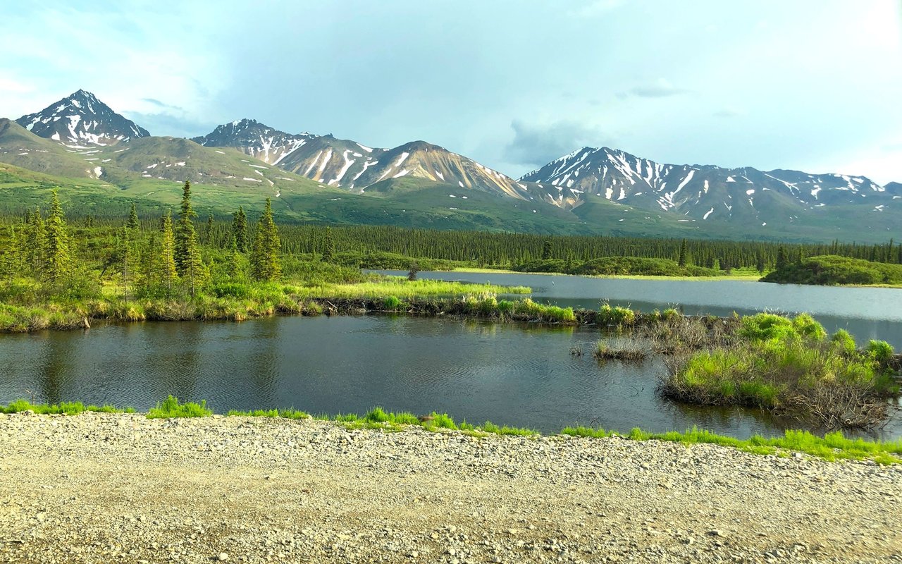Mountain landscape near Sutton, Alaska, with snow-streaked peaks, evergreen forest, and a pond.