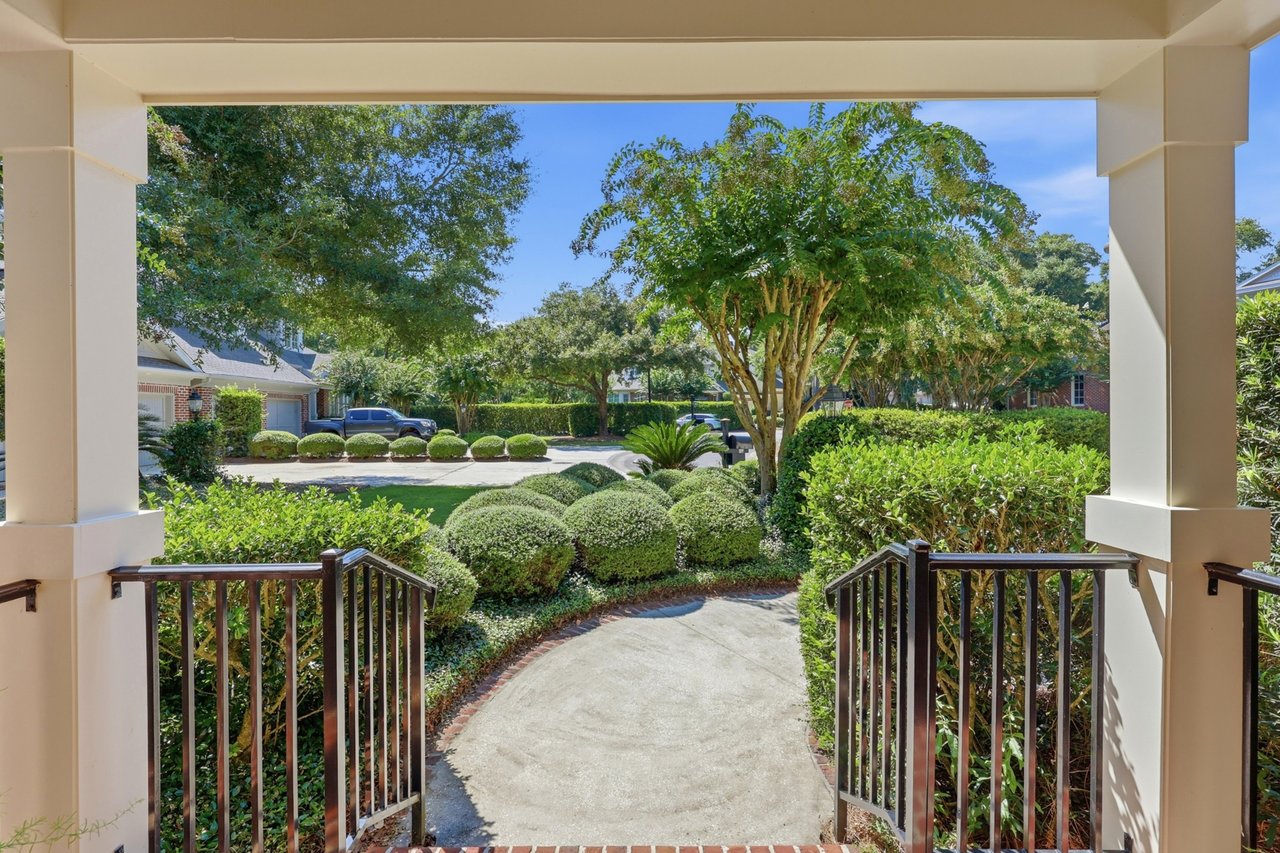 Walkway from a covered entrance toward a landscaped street, framed by railings and trimmed shrubs.
