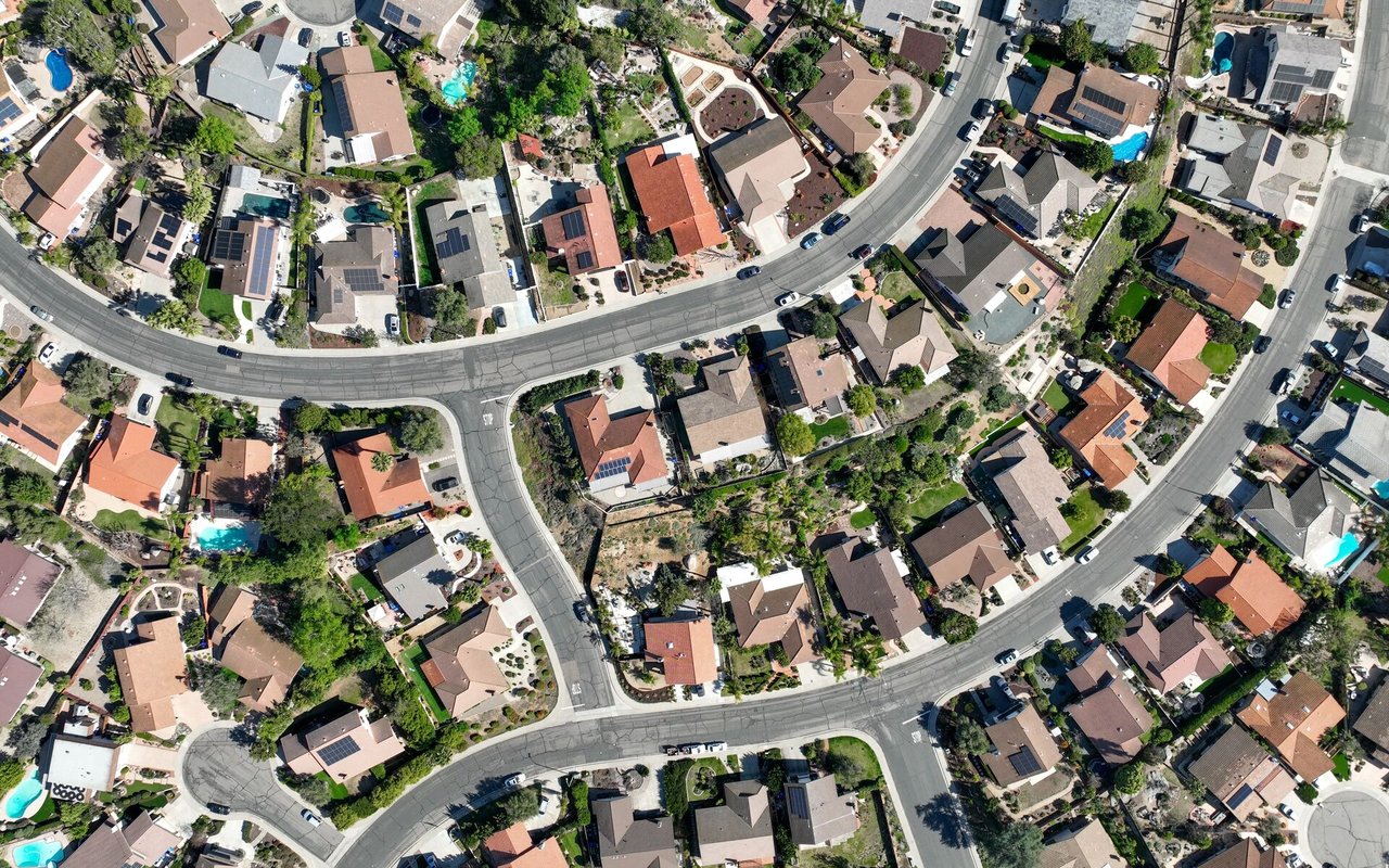 Aerial view of a residential neighborhood with curving streets, swimming pools, and solar panels.