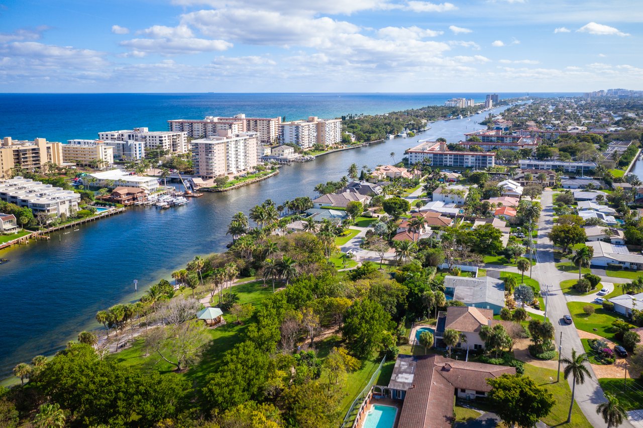 Aerial view of a coastal neighborhood, with homes along a canal opening toward the ocean.