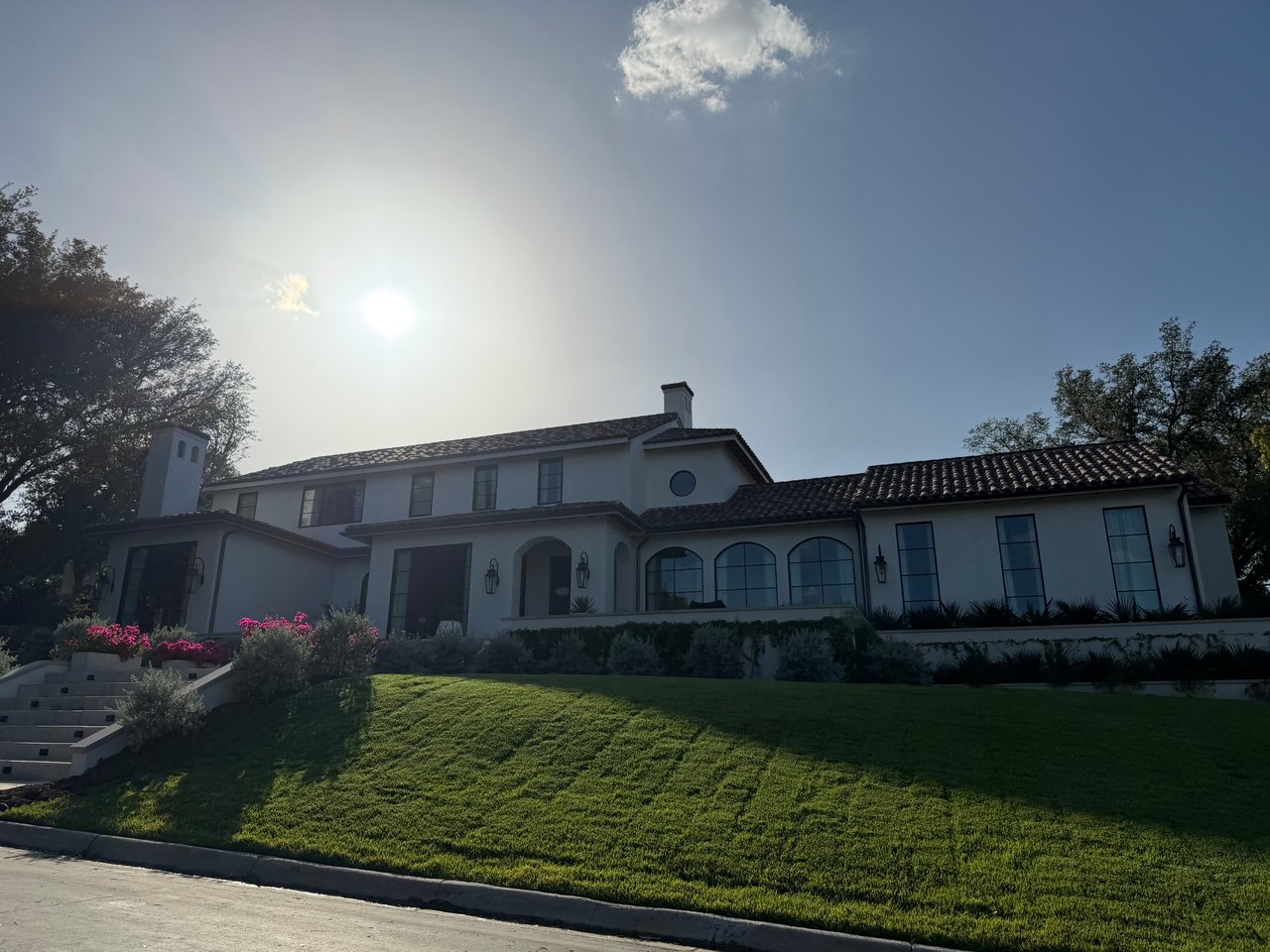 Large stucco house with a tile roof, arched windows, and a landscaped front lawn.