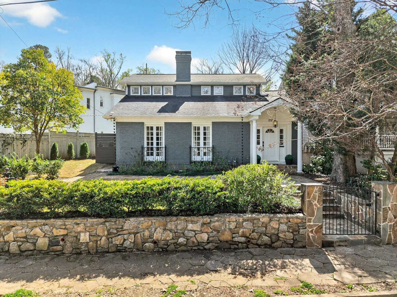 Gray brick house with white trim, landscaped shrubs, and a stone retaining wall along the front walk.