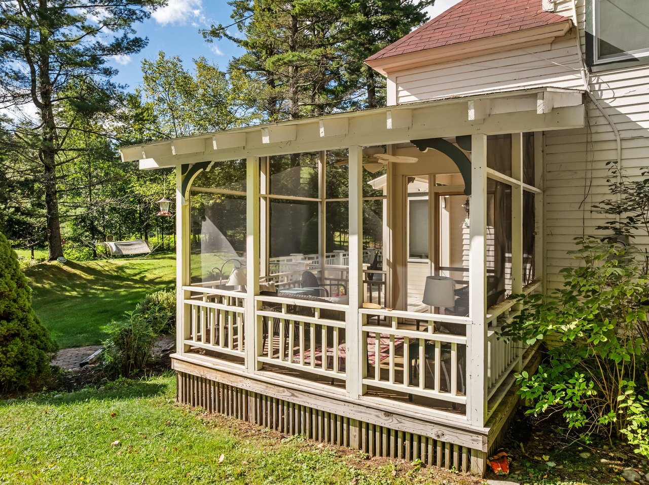 Screened porch on a white-sided cottage overlooking a shaded lawn and trees.