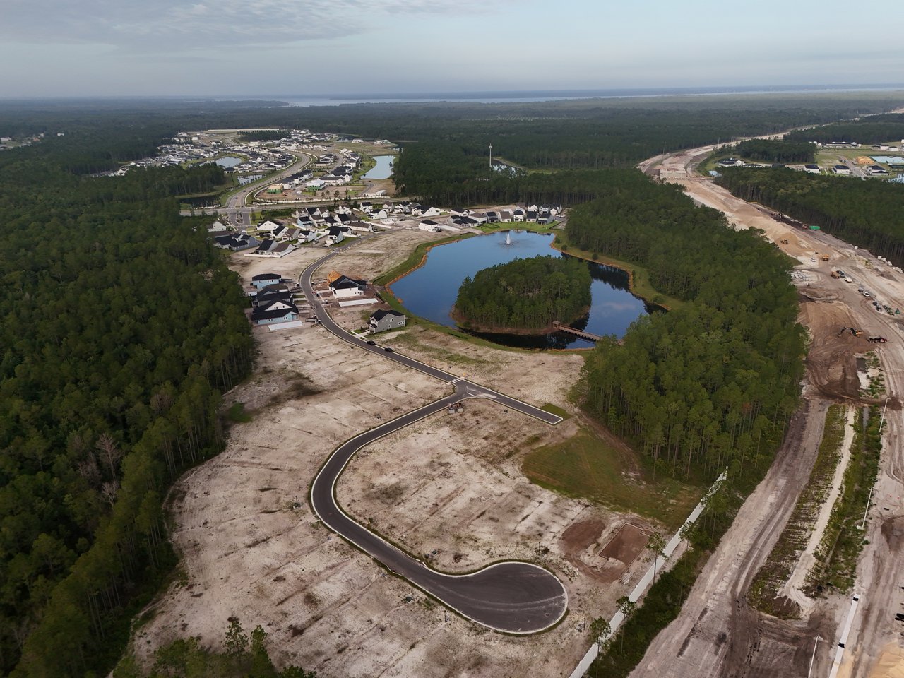 Aerial view of homes around a lake, with wooded land and construction roads nearby.