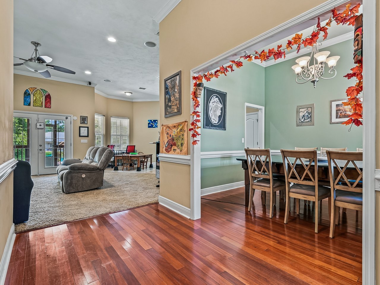 Open-plan living and dining area with hardwood floors, a gray reclining sofa, and an autumn-decorated dining room.