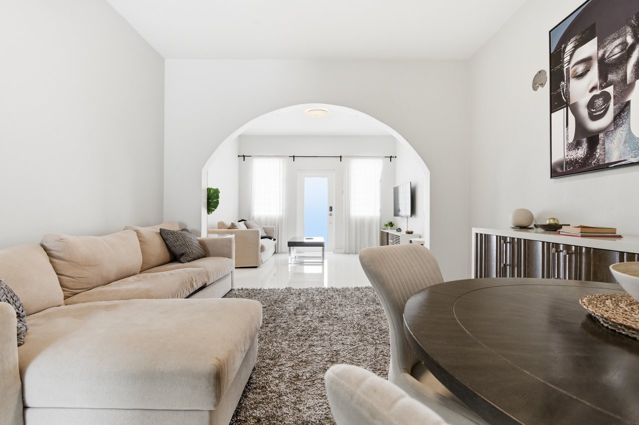 Living and dining room with a beige sectional, round dark table, shag rug, and arched opening.