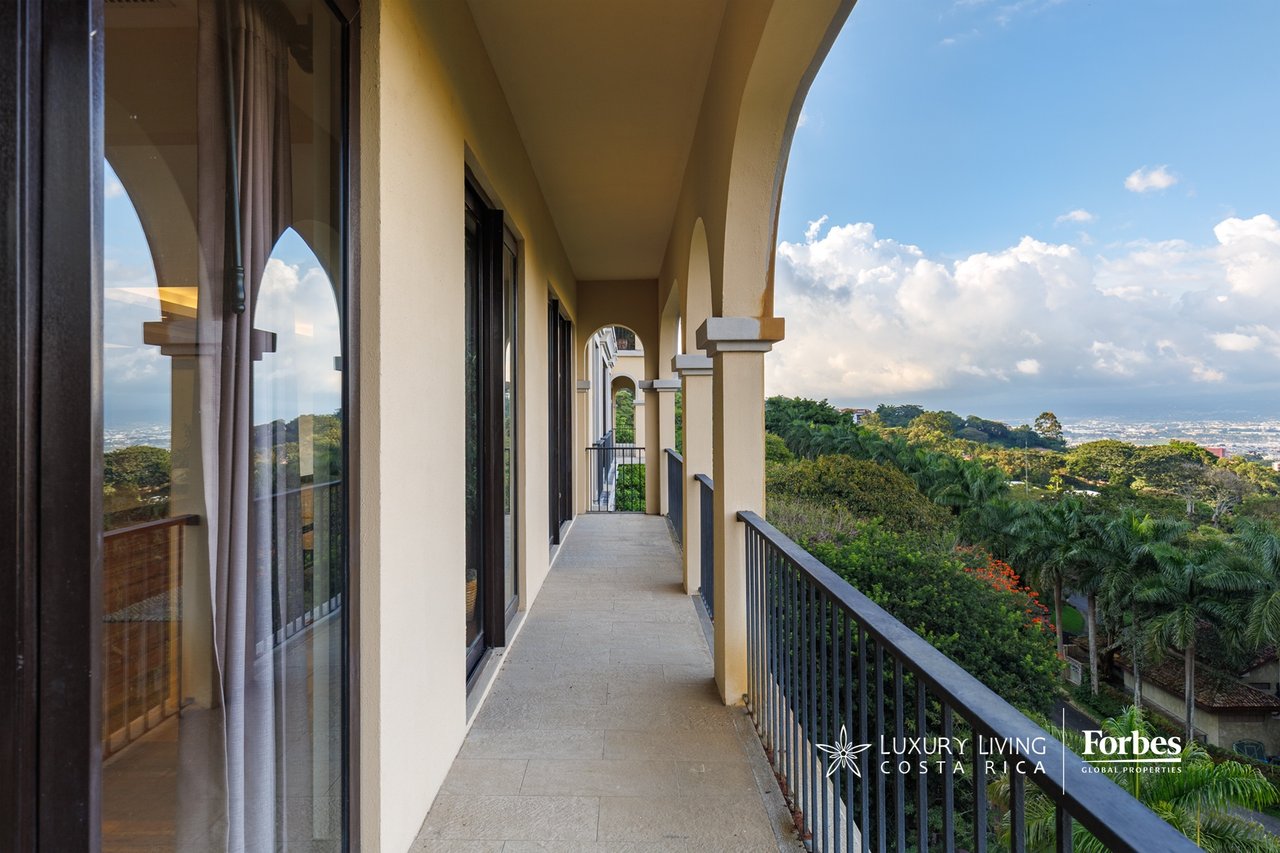 Penthouse balcony with arched columns and views over tropical greenery and the city valley.