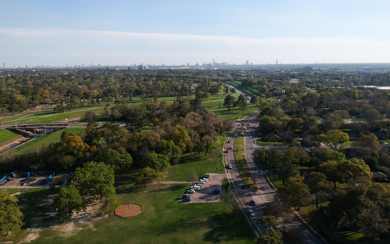 Aerial view of a Houston park and neighborhood, with downtown skyline in the distance.