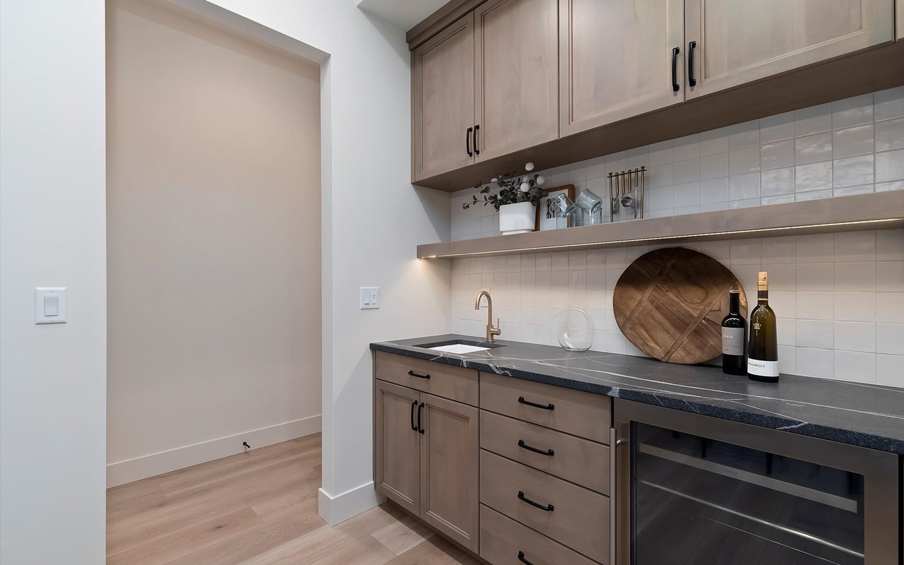 Wine bar with sink, leathered granite countertop and under-cabinet lighting.