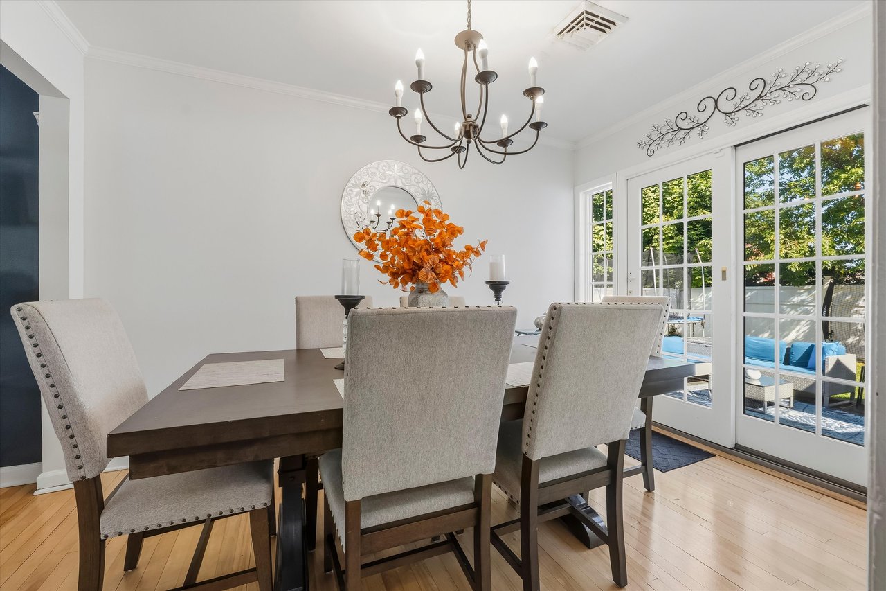 Dining room with a dark wood table, upholstered chairs, chandelier, and French doors opening to a patio.