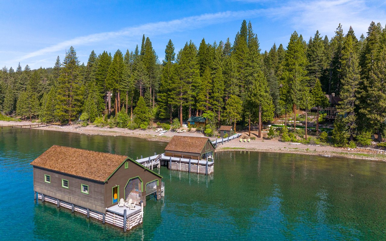 Lakefront boathouses along a pine-covered West Lake Tahoe shoreline.
