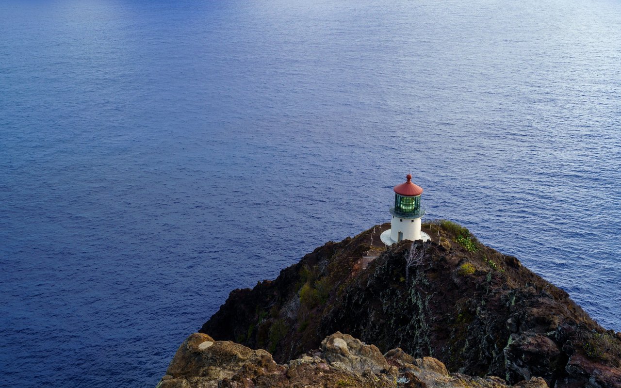 White lighthouse with a red roof on a rocky point above the ocean.