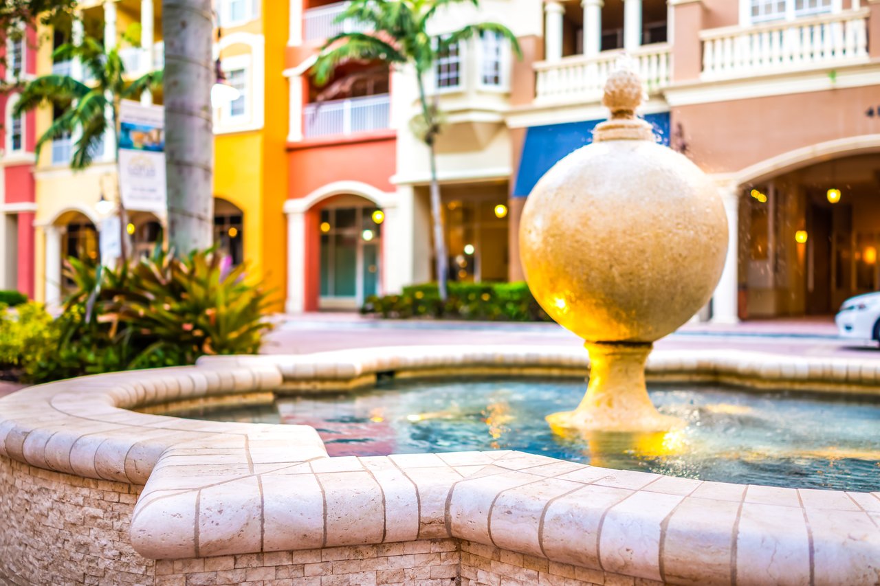 Courtyard fountain in front of colorful Mediterranean-style facades and palm trees.