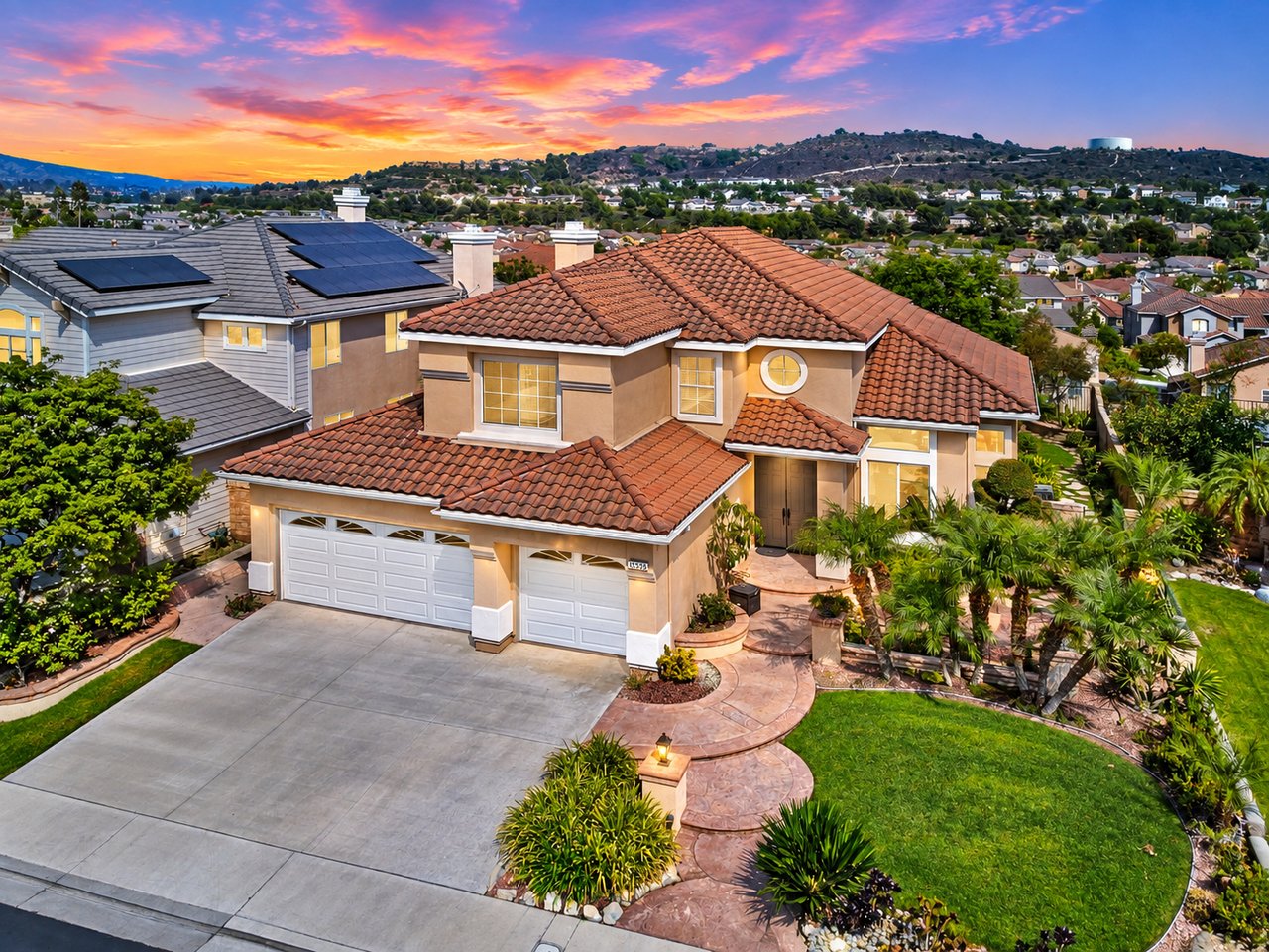 Two-story home with a terracotta tile roof, double garage, and landscaped front yard at sunset.