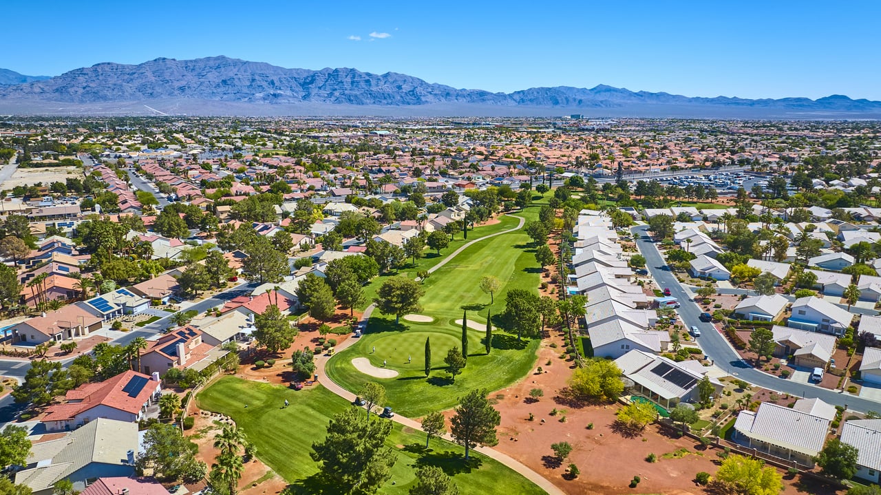 Aerial view of a Las Vegas residential neighborhood with homes surrounding a golf course and the Spring Mountains in the background.