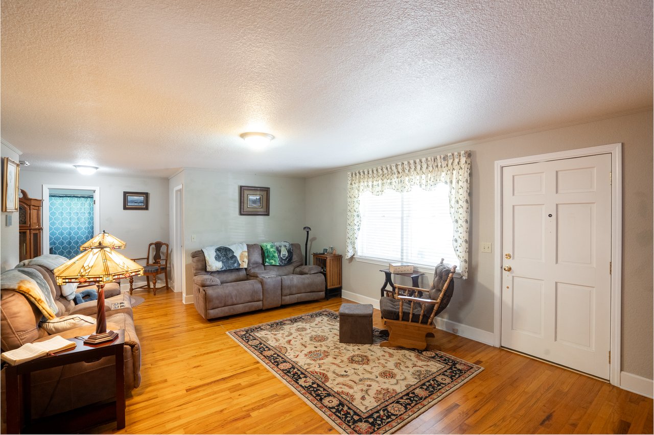 A cozy living room features two sofas, a rocking chair, and a rug on hardwood flooring. Lamps and pictures decorate the space, while a window with curtains lets in natural light—a perfect setting for real estate agents to visualize inviting homes for their clients.