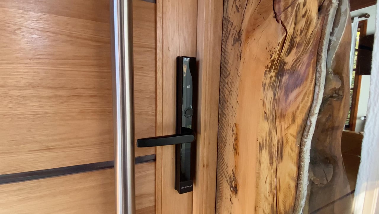 Wooden entry door with a black smart lock and live-edge timber frame.