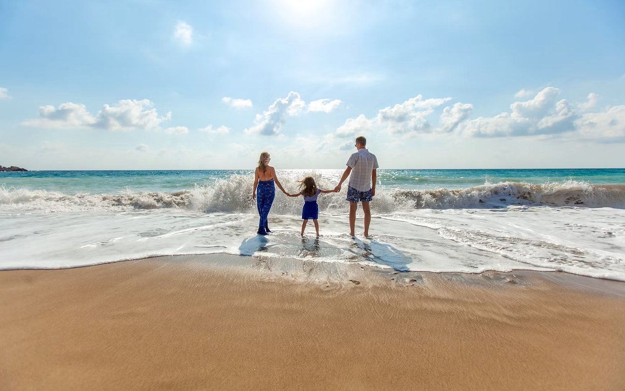 Family holding hands in the surf on a sunny beach.