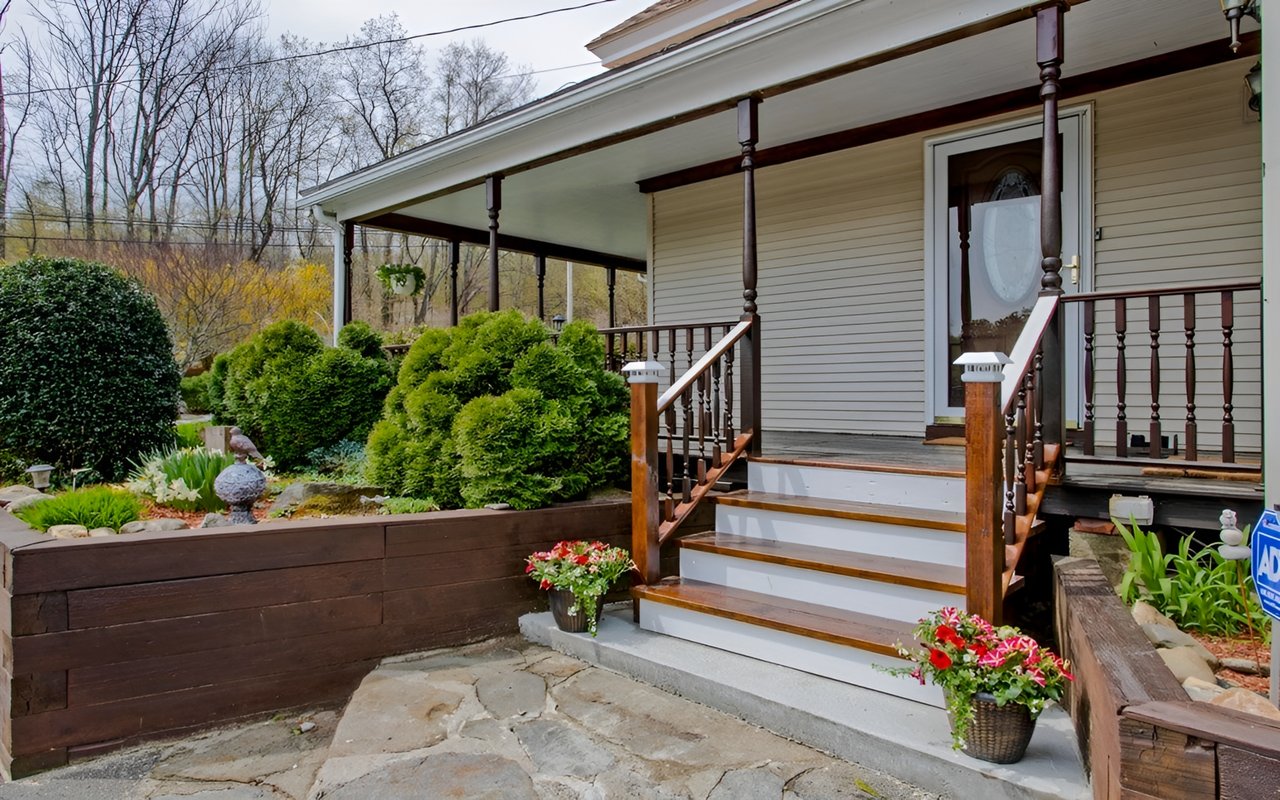 House entrance with a covered porch, white steps, dark wood railings, and flower planters.