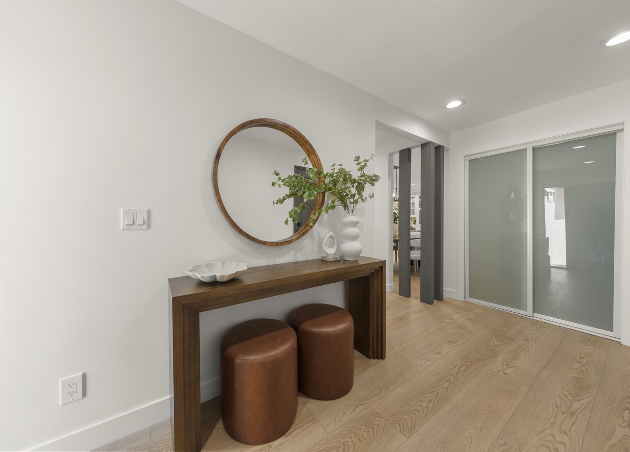 Entryway with a wood console, two leather stools, round mirror, and sliding glass doors.