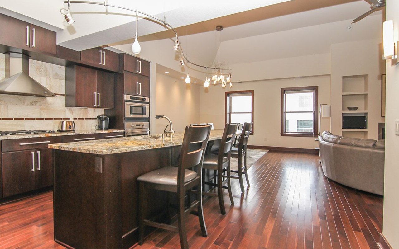 Open-plan kitchen and living area with dark wood cabinetry, granite island, and hardwood floors.