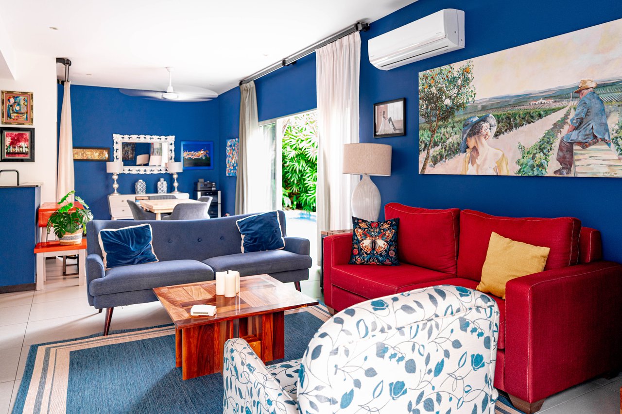 Furnished living room with blue walls, red and gray sofas, and a dining area.