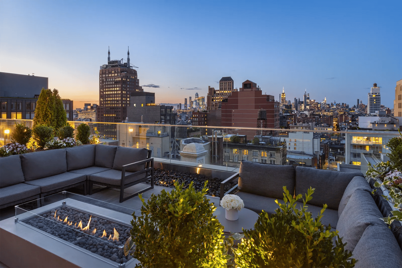 Rooftop terrace with sectional seating and a fire feature overlooking the New York City skyline at dusk.