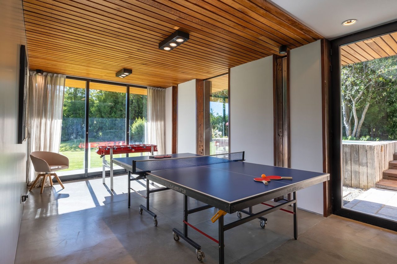 Game room with a ping-pong table, foosball table, and garden views through glass doors.