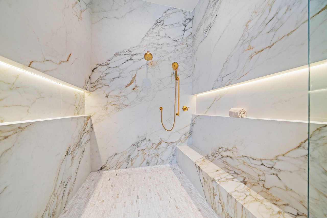 Marble walk-in shower with a built-in bench and polished gold fixtures.