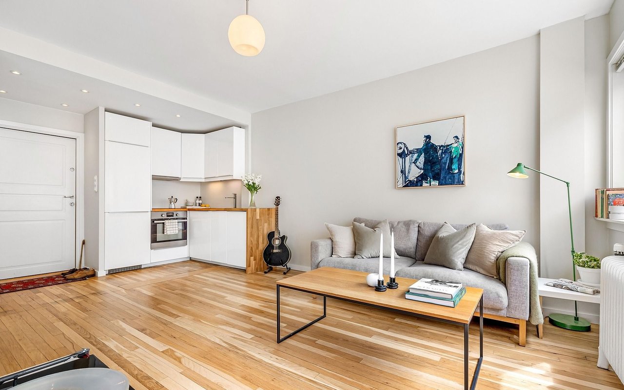 Open-plan living room and kitchen with a gray sofa and light hardwood floors.