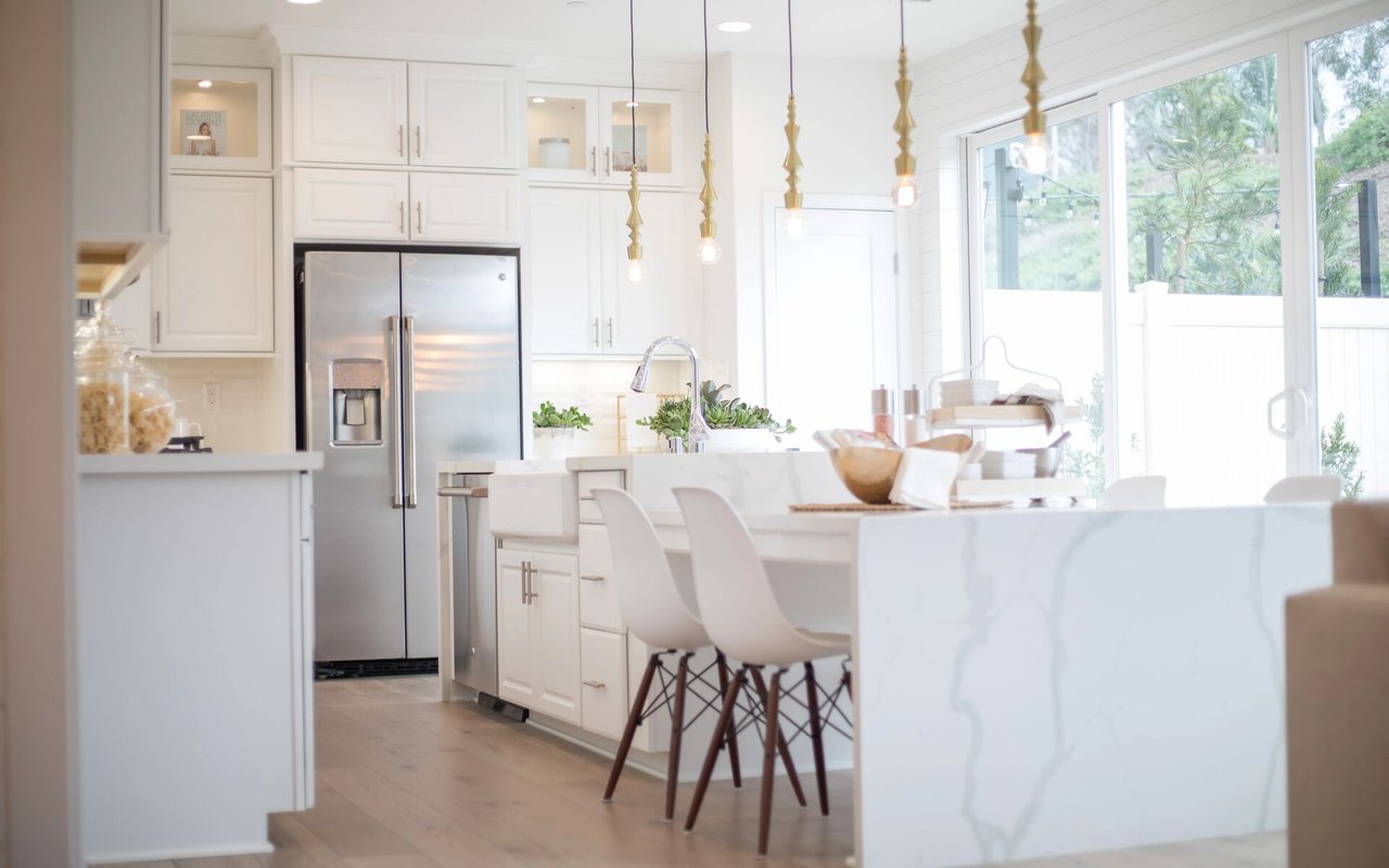 Bright white kitchen with a marble-look island, brass pendants, and large windows.