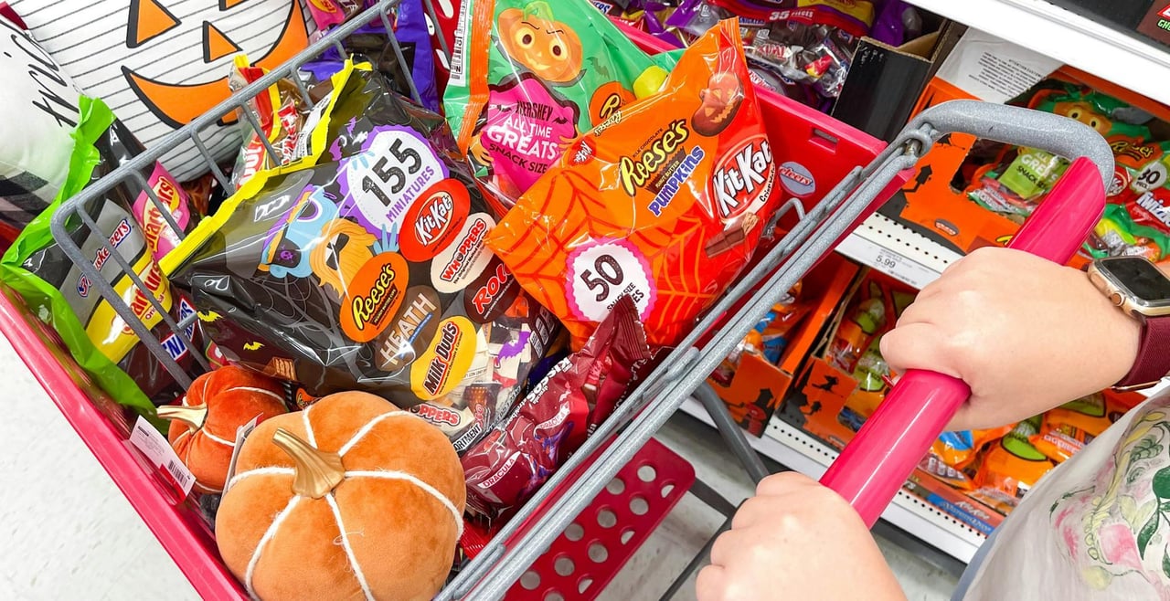 Halloween shopping basket filled with candy, costume accessories, and small seasonal decorations.