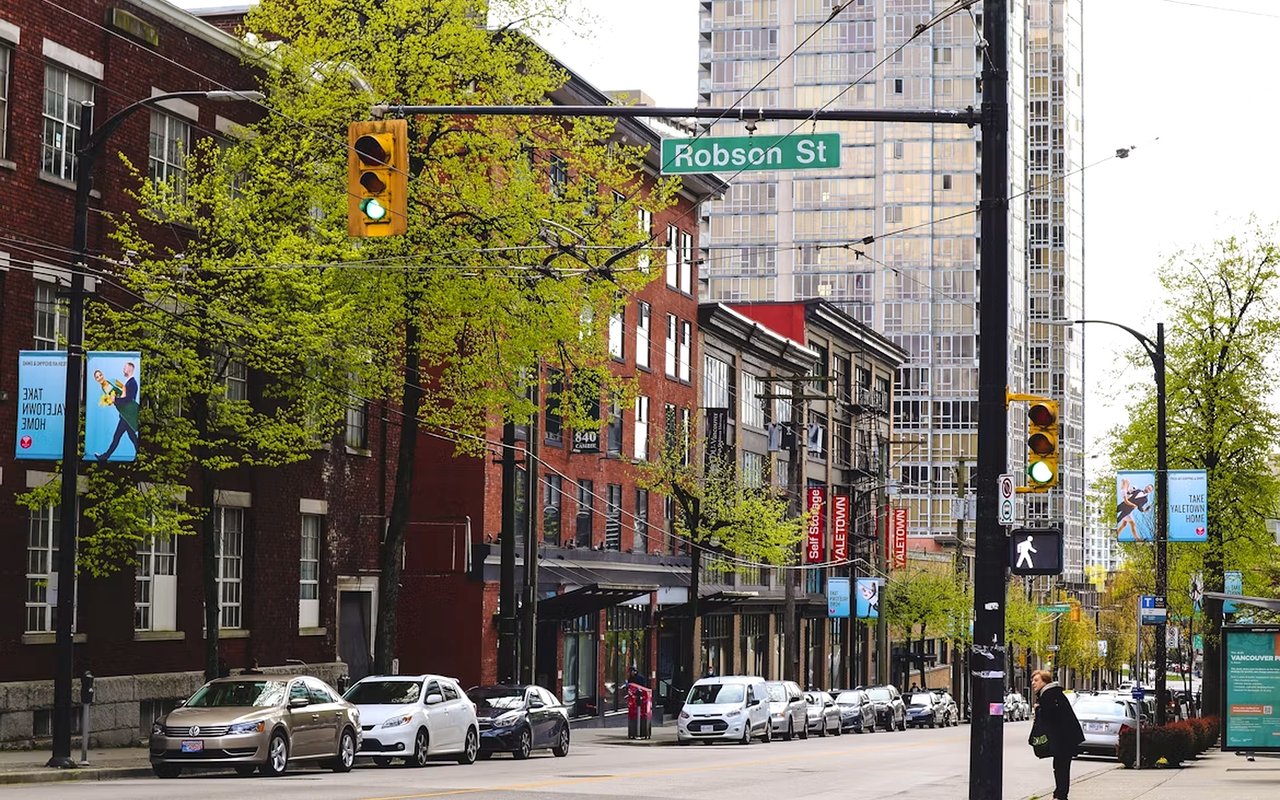 Robson Street in Vancouver, lined with brick storefronts and high-rise buildings.