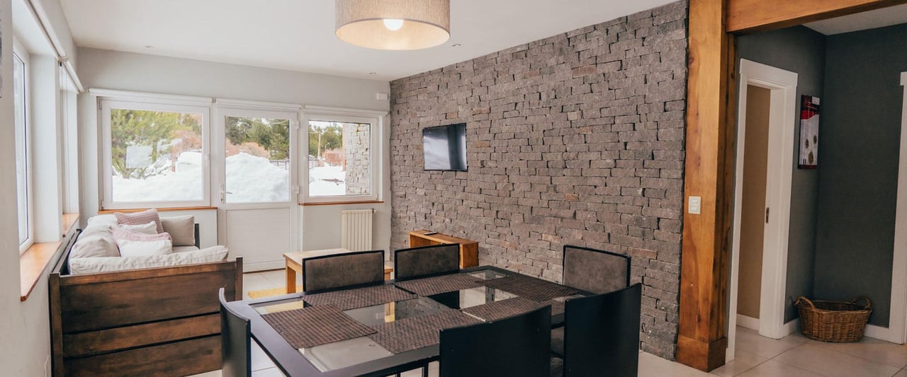 Living and dining area with a stone accent wall and snow visible through the windows.