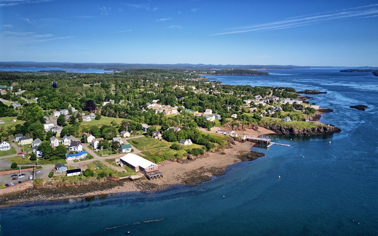 Coastal community with scattered houses, a rocky shoreline, and blue water.