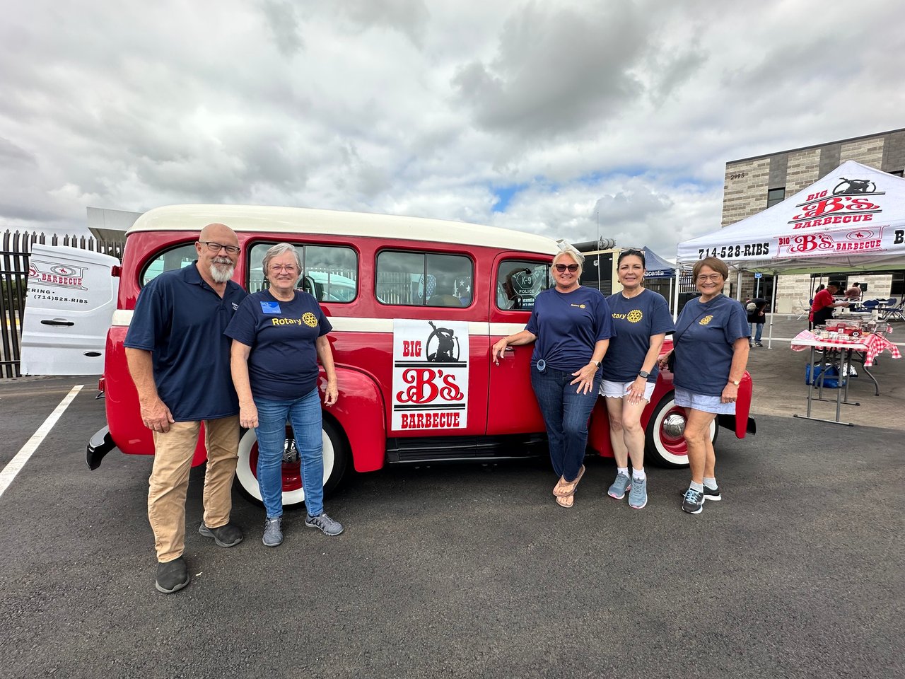 Six Rotary members pose beside a red-and-white Big B’s Barbecue truck.