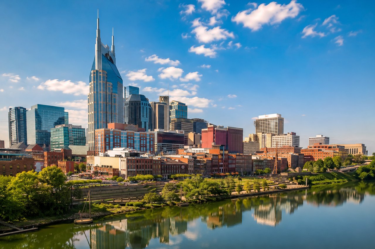 Downtown Nashville skyline overlooking the Cumberland River on a sunny day, representing Tennessee's thriving economy, luxury real estate market, and the appeal of relocating for lower taxes and an exceptional quality of life.