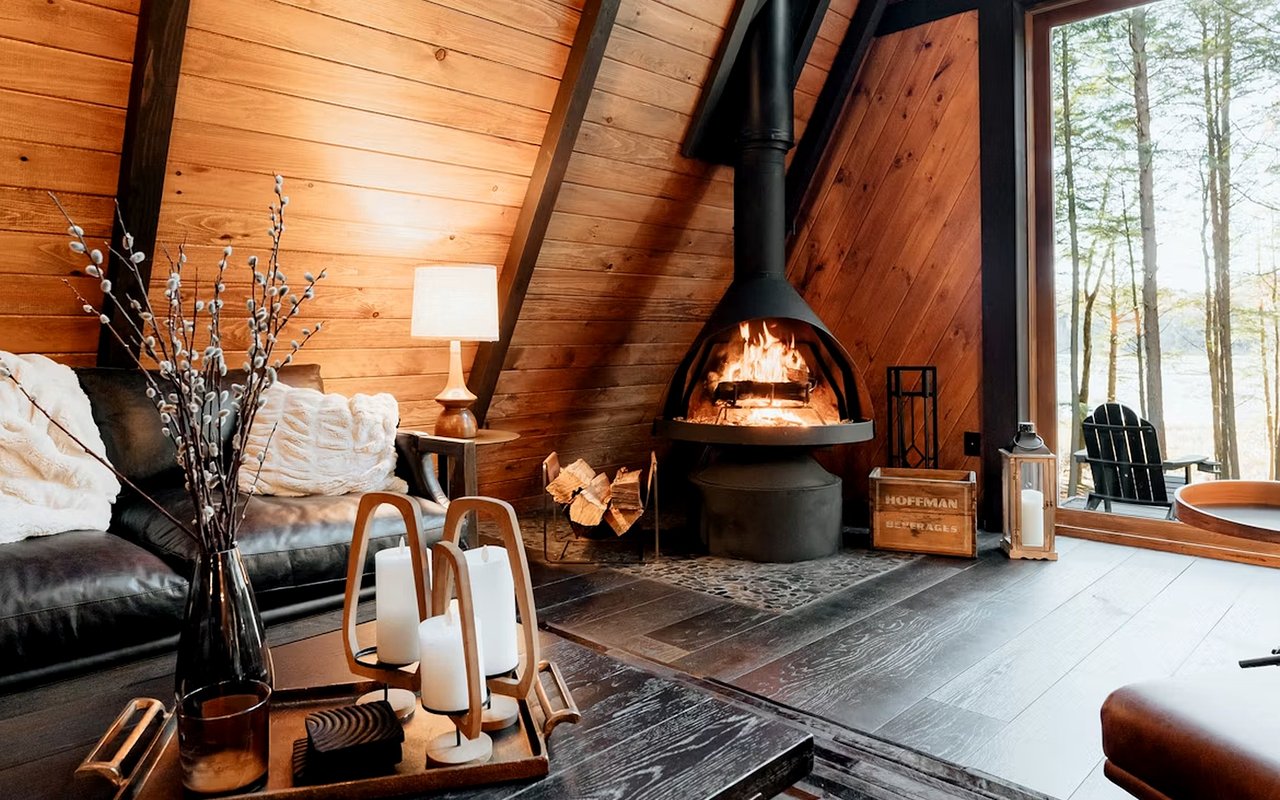 Living room with a lit suspended fireplace, vaulted wood ceiling, and large windows.