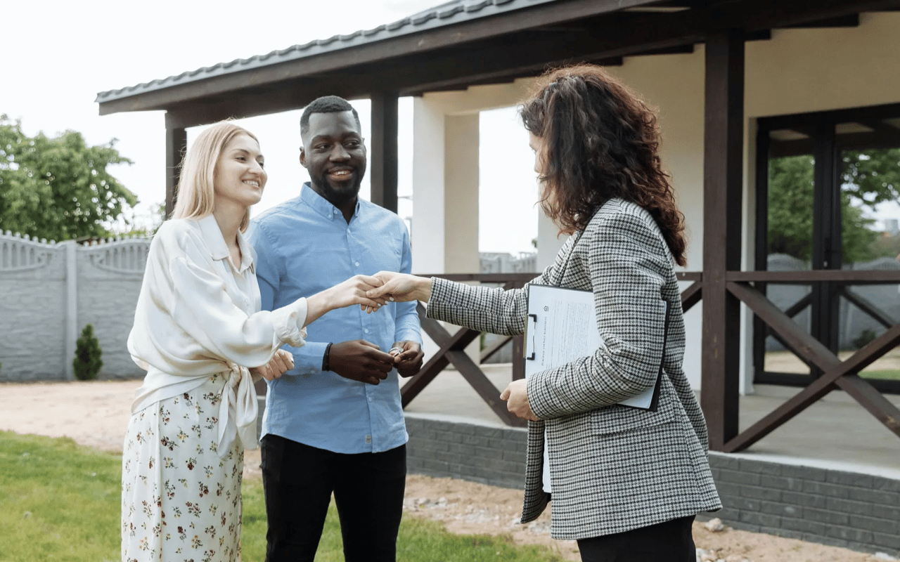 Real estate agent greets a couple outside a modern home.
