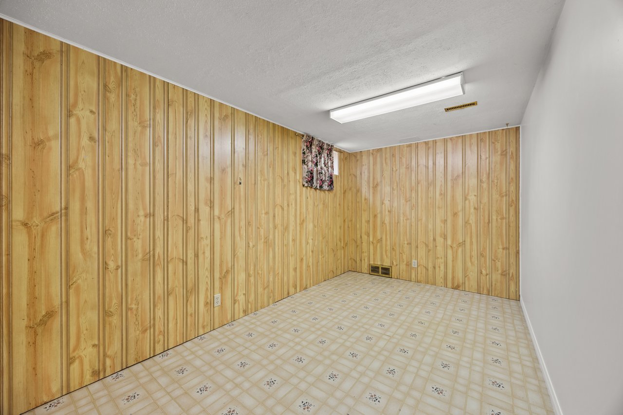 Empty room with wood-paneled walls, patterned vinyl flooring, and a fluorescent ceiling light.