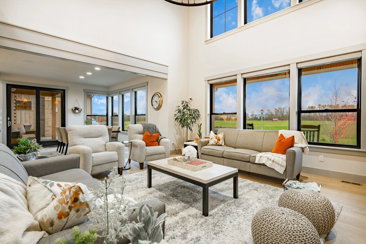 Double-height living room with cream sofas and large windows overlooking green fields.