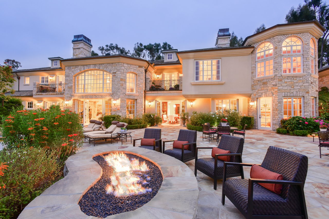 Stone-and-stucco home with a curved patio fire pit and outdoor seating at dusk.
