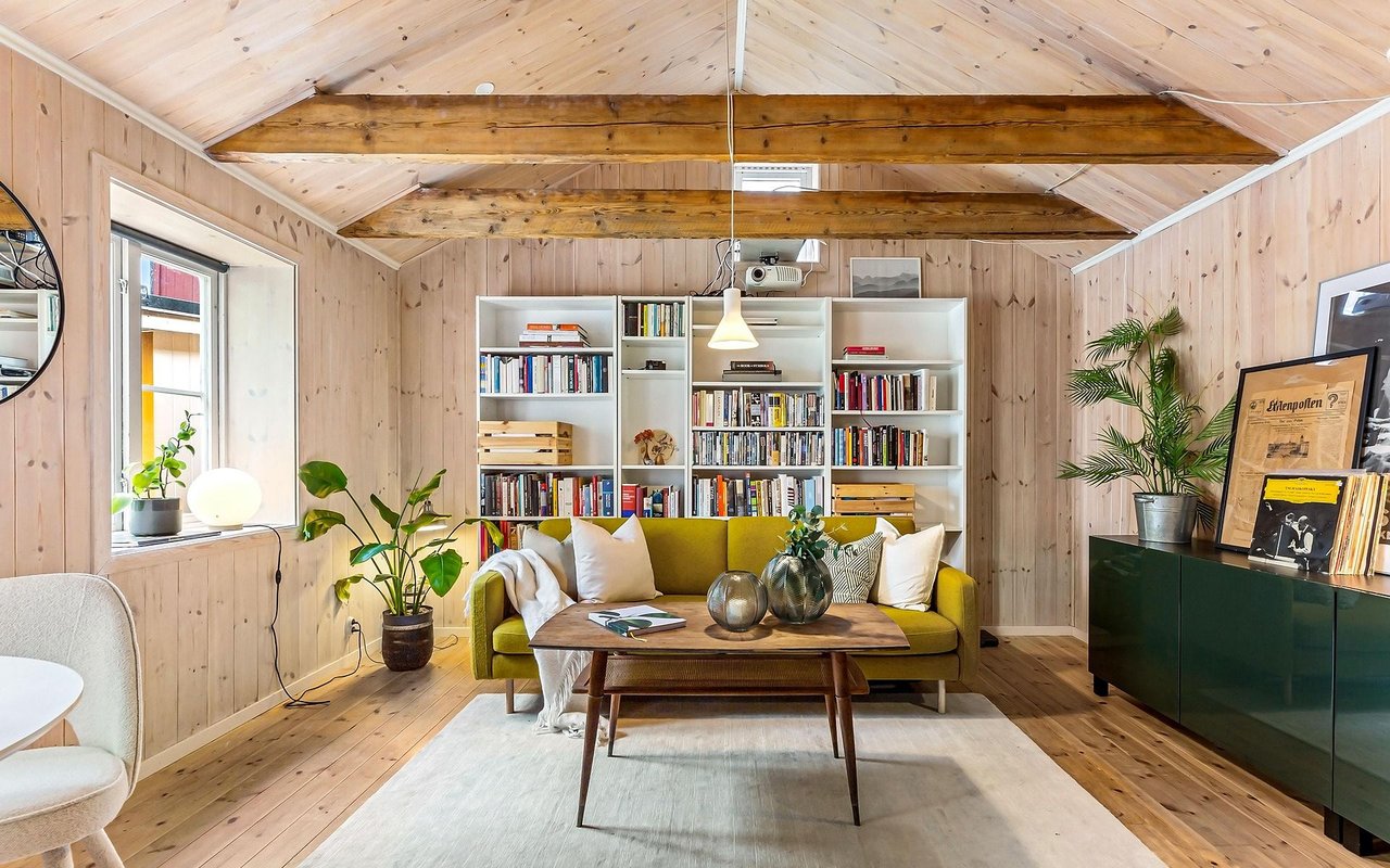 Wood-paneled living room with exposed ceiling beams, a mustard sofa, and bookshelves.