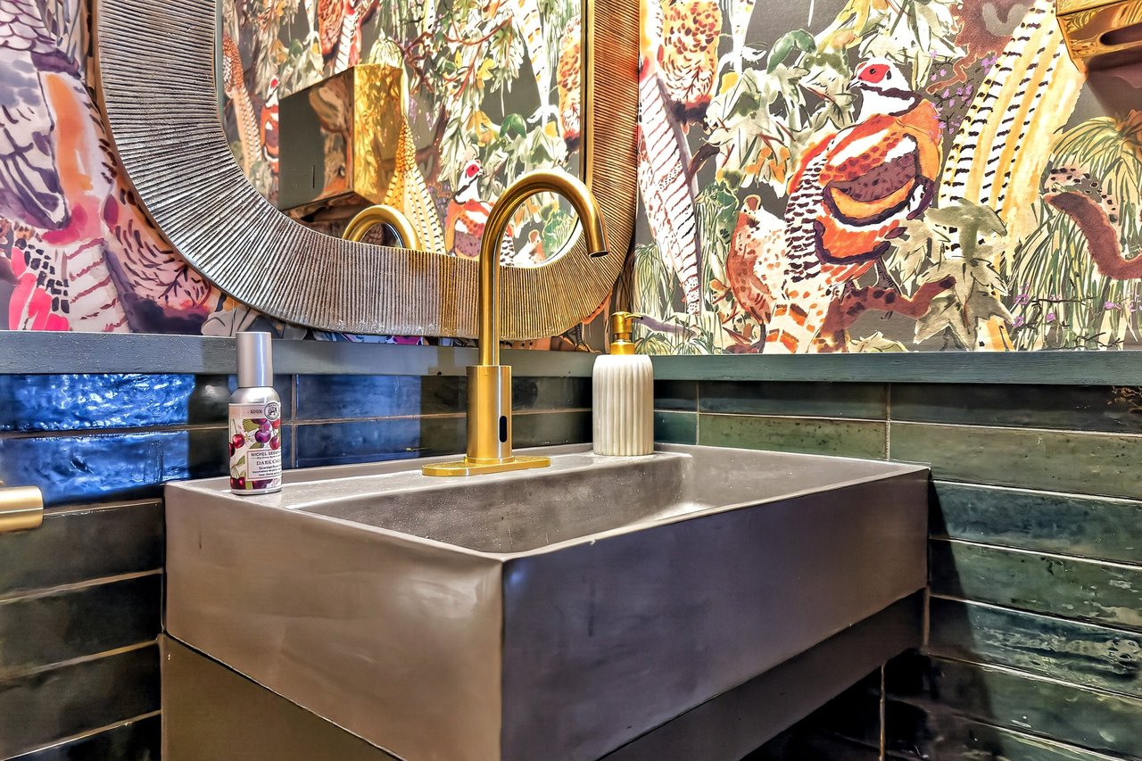 Restaurant bathroom vanity with a rectangular sink, gold faucet, and colorful bird-patterned wallpaper.